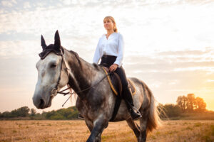 mujer montando un caballo gris en un campo al atardecer. caminar, montar a caballo, alquiler. Hermoso fondo, la naturaleza al aire libre. entrenamiento deportivo ecuestre.